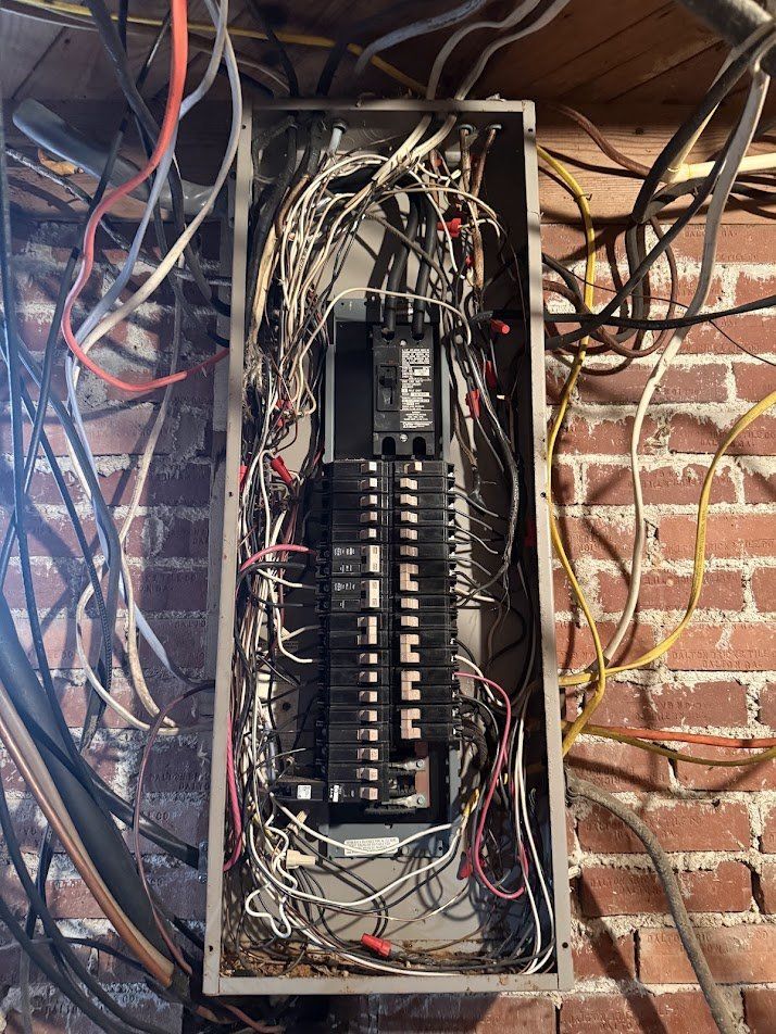 Overcrowded old panel with tangled wiring on a brick basement wall